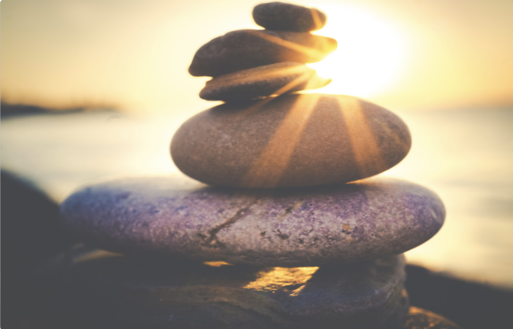 This is an image of rocks stacked up on a beach, with a sunset in the background.
